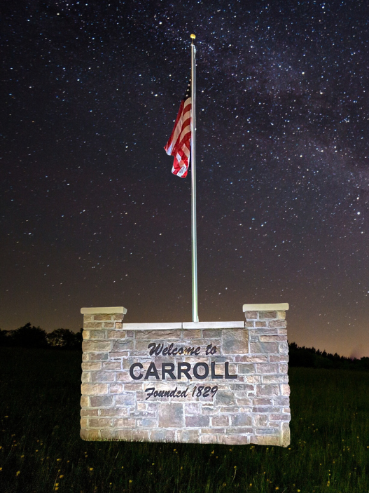 Welcome to Carroll, Founded 1829 stone sign with an American flag at night